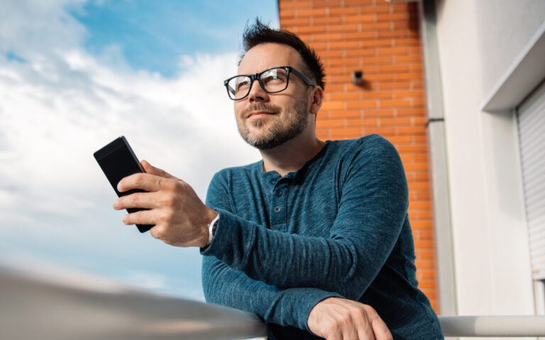 Man with glasses using smart phone outdoor. He is wearing blue shirt.